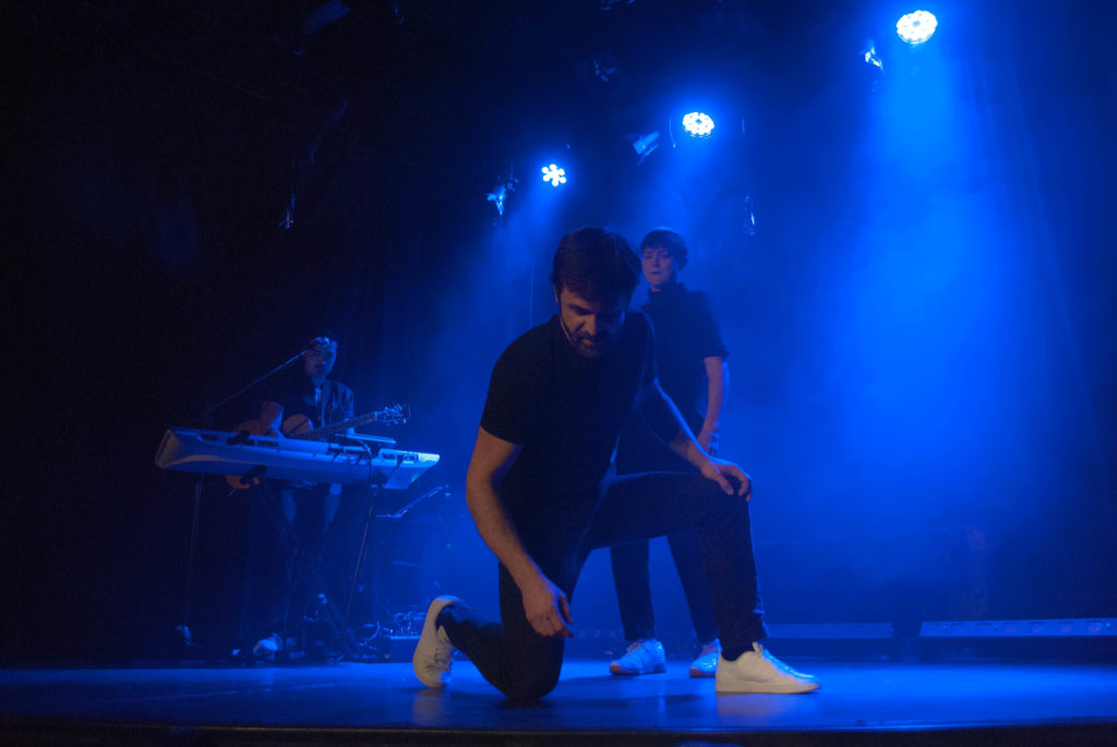 Cédric Fernandez accroupit au sol, avec Julie Gallibert et William Babin derrière pour illustrer le théâtre d'impro' en entreprise
