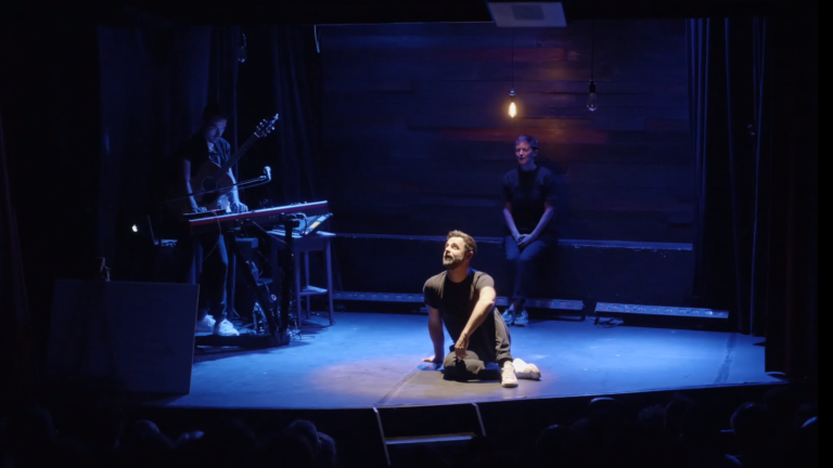 Cédric Fernandez, assit au milieu de la scène du Grand Point Virgule, avec Julie Gallibert derrière lui et William Babin à la musique durant Expérience Inoubliable